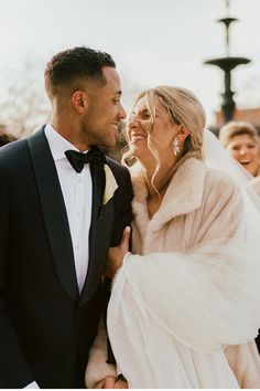 a bride and groom smile at each other as they stand in front of the crowd