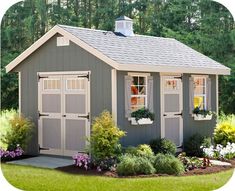 a small gray shed with windows and flowers