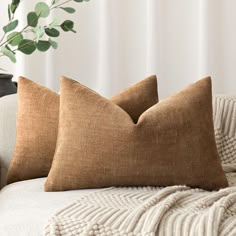 two brown pillows sitting on top of a white couch next to a potted plant