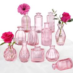 pink glass vases with flowers in them on a white surface