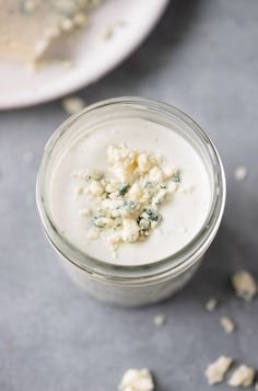 a glass jar filled with cheese on top of a gray table next to a white plate