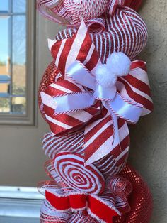 a red and white christmas wreath hanging from the side of a building with ribbons on it