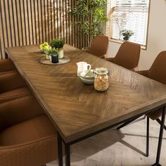 a wooden table with chairs around it in front of a plant and potted plants