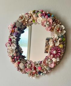 a mirror that is hanging on the wall with flowers in it and beads around it