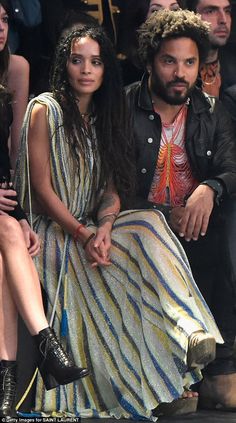 a man and woman sitting next to each other at a fashion show with people in the background