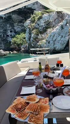 a table with food and drinks on it in front of a boat near the water