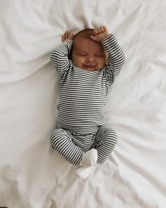 a baby laying on top of a white bed next to a stuffed teddy bear wearing a green and white striped outfit