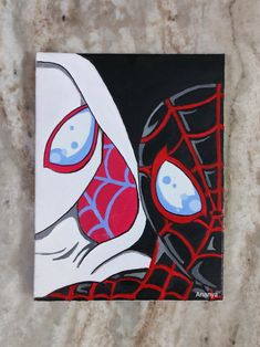 a painting of a spider man with red and blue eyes on a black square piece of paper