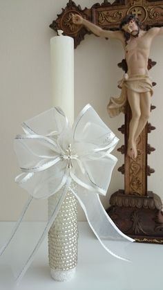 a candle with a white ribbon around it next to a cross and statue in the background