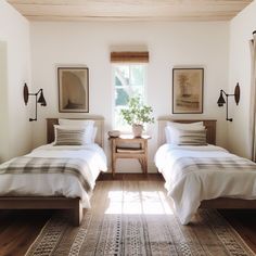 two beds in a room with wooden floors and white walls, one has a plant on the end table