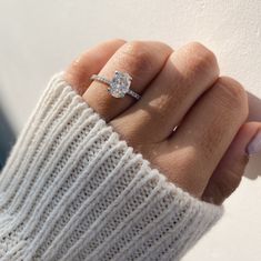 a woman's hand with a diamond ring on her finger, wearing a white sweater