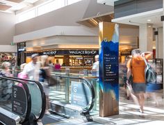 people are walking through an airport terminal with escalators and signs on the walls