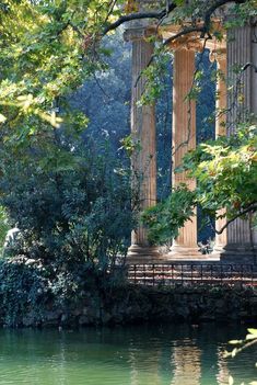 an old building with columns next to a body of water in front of some trees