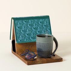 a coffee cup sitting on top of a wooden stand next to a pair of sunglasses