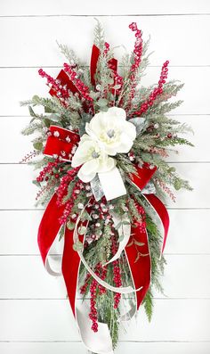 a red and white christmas wreath hanging on the side of a wall with greenery