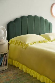 a bed with yellow ruffled bedspread next to a book shelf and round window