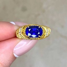 a woman's hand holding a ring with a blue stone in the middle and gold trimmings