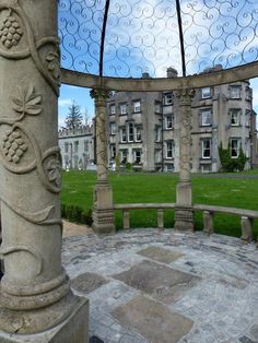 an old building with a glass roof and stone pillars in the foreground, surrounded by green grass