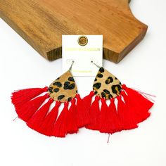 Leopard teardrop earrings with tassels trim in red. Pictured on a white background with a wood piece at the top. Trendy Red Tassel Earrings, Trendy Fringe Tassel Dangle Earrings, Trendy Tassel Dangle Earrings With Fringe, Trendy Tassel Earrings, Trendy Tassel Drop Earrings, Trendy Tassel Fringe Drop Earrings, Red Fringe Tassel Earrings As Gift, Red Latkans Tassel Earrings For Gifts, Trendy Tassel Drop Earrings With Fringe