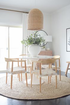 a dining room table with chairs and a vase on top of it in front of a window