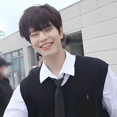 a young man wearing a black vest and tie smiles at the camera while standing in front of a building