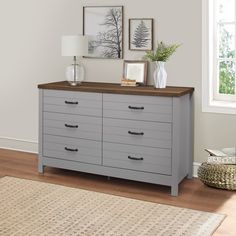 a gray dresser with drawers and pictures on the wall above it in a living room