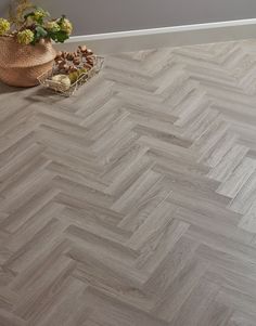 a vase with flowers on the floor in front of a window and a wooden herringbone pattern