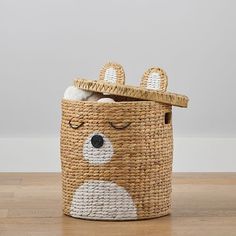 a basket with a bear face painted on the front and sides, sitting on a wooden floor