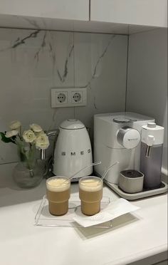 there are two cups on the counter next to some coffee maker and blender in front of them