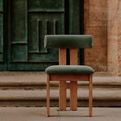 a wooden chair sitting on top of a sidewalk next to a green door and steps