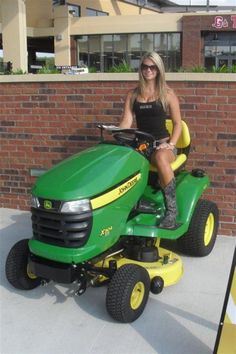 a woman sitting on top of a green lawn mower