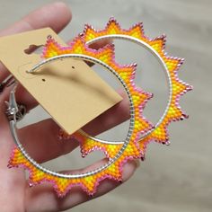 a hand holding a pair of hoop earrings with an orange and yellow design on it