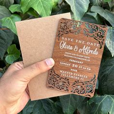 a person holding up a wooden save the date card in front of some green leaves