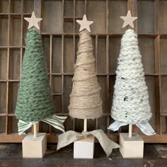 three small christmas trees are on display in front of a wooden box with twine