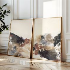 two framed paintings sitting on top of a wooden floor next to a potted plant