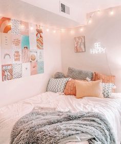 a white bed topped with lots of pillows next to a wall covered in pictures and lights