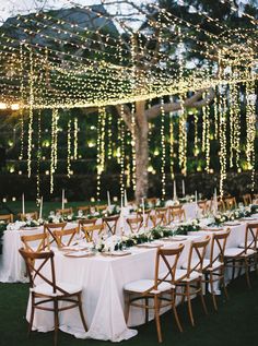 an outdoor dinner table set up with white linens and lights strung from the ceiling