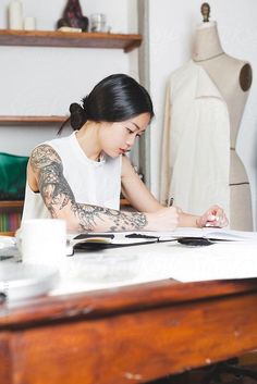 a woman sitting at a table writing on a piece of paper by some mannequins