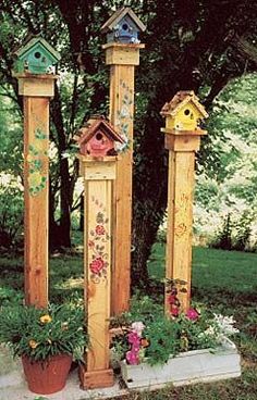 three tall wooden birdhouses with flowers and birds on them in the grass near some trees