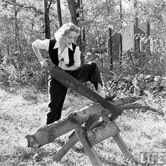 an old woman sitting on top of a piece of wood with a saw in her hand