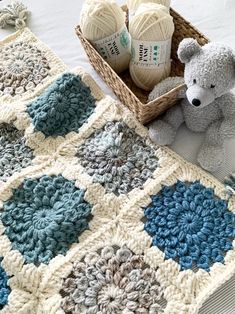 a crocheted blanket and two balls of yarn next to a teddy bear on a bed