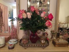 a vase filled with pink roses sitting on top of a table next to a mirror