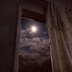 the full moon is seen through an open window in a dark room with white curtains