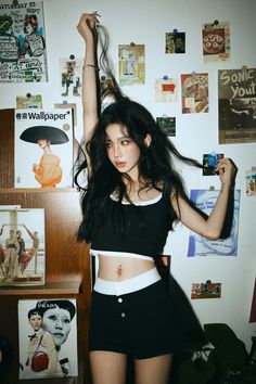 a woman with long black hair standing in front of a wall full of pictures and posters