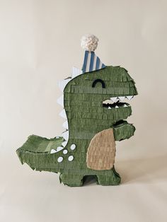 a paper cut out of a green dinosaur with a party hat on it's head