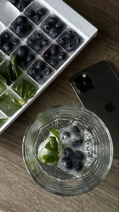 a glass filled with blueberries and mint next to an iphone on a wooden table