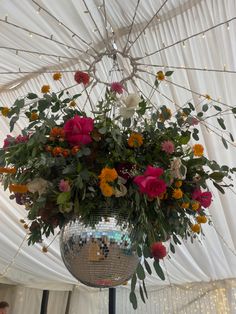 a disco ball filled with flowers and greenery hanging from the ceiling in a marquee