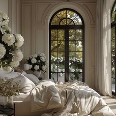 a bed with white sheets and pillows in front of an arched window that has flowers on it