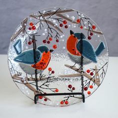 a glass plate with two birds perched on branches and berries in the background, sitting on a table