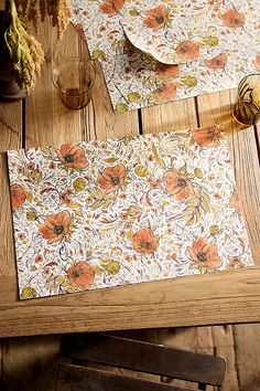 two placemats with flowers on them sitting on a wooden table next to a vase